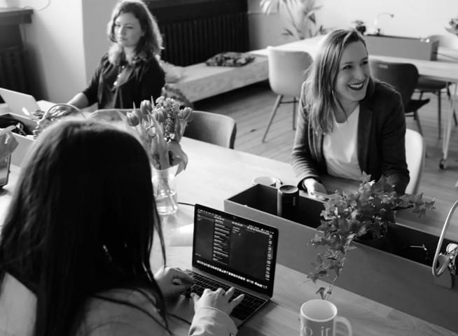 Three female data analysts working sitting at the table in front of their computers and one of them is smiling